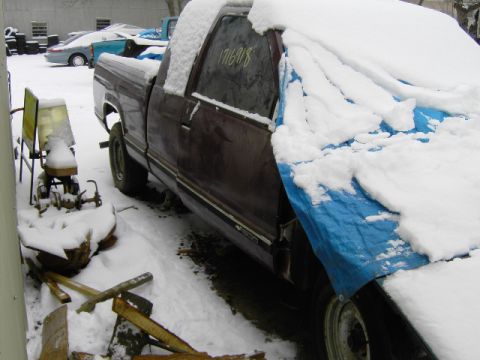 1991 Ford Bronco - A maroon truck sits partially covered in snow and a blue tarp in a snowy yard with other vehicles visible.