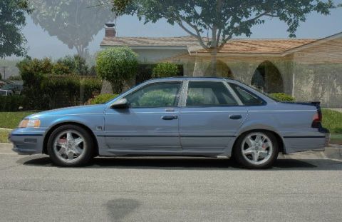 1993 Ford Taurus - A blue sedan with custom wheels is parked on a residential street.