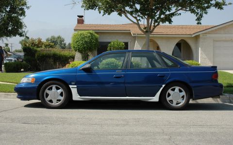 1993 Ford Taurus - Side view of a blue sedan with white lower body trim parked on a residential street.