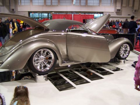 1995 Ford Probe - A silver customized hot rod is displayed with its doors and hood open, its chrome wheels and custom bodywork.