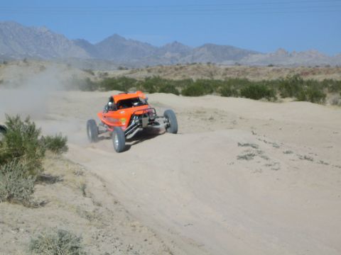 Orange off-road race buggy on a desert course with mountains behind