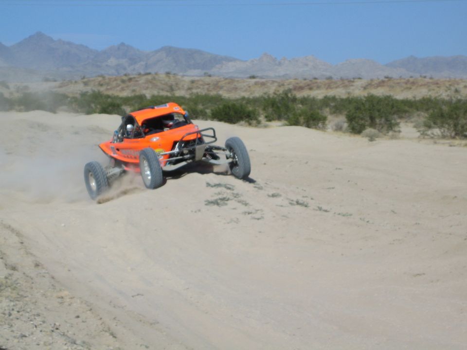 Orange off-road race buggy catching air over a desert rise