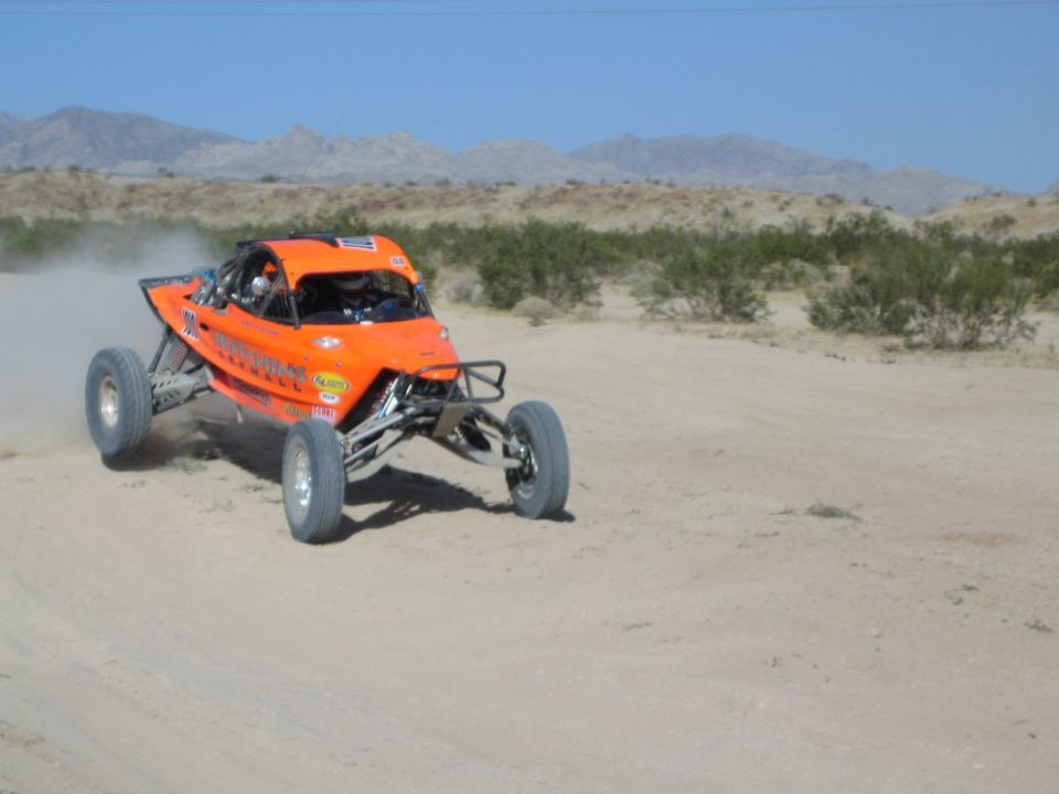 Orange off-road race buggy speeding on a desert track near mountains
