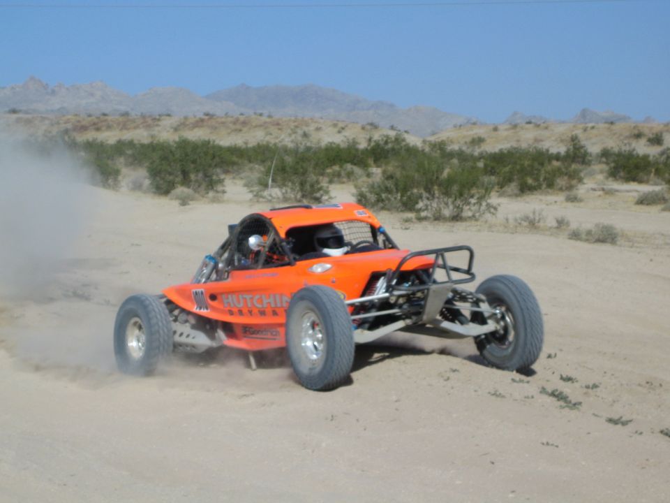 Orange off-road race buggy with Hutchins lettering on a desert course