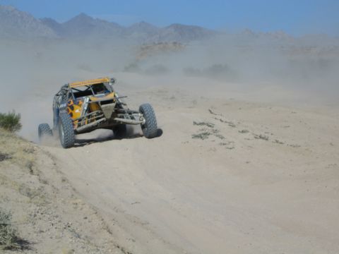 Yellow off-road race buggy throwing dust on a desert course with mountains