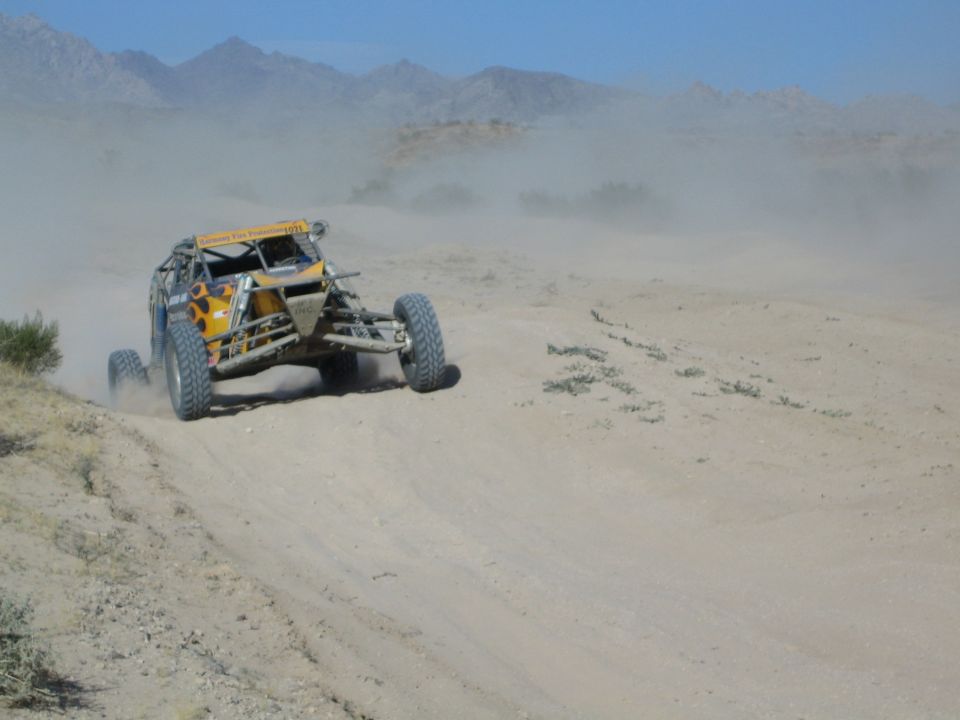 Yellow off-road race buggy throwing dust on a desert course with mountains