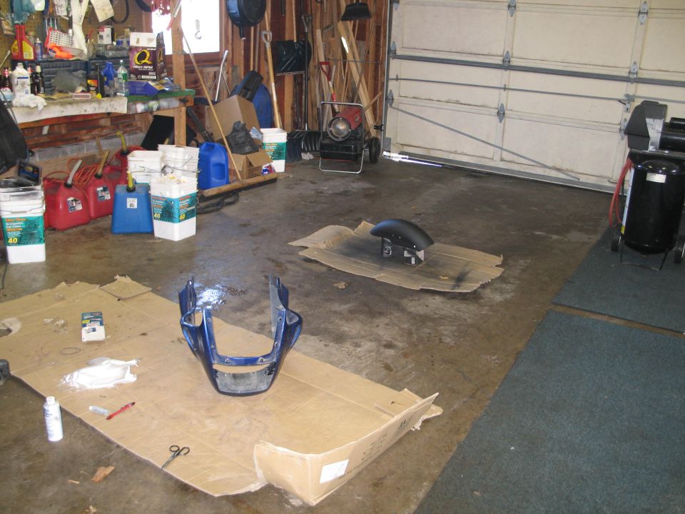 Blue motorcycle front fairing and black front fender laid on cardboard in a garage