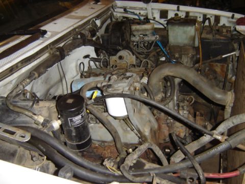 1992 Ford Bronco - The engine bay of a vehicle is shown, various hoses, a filter, and other mechanical components.