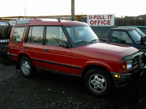 1996 Land Rover Discovery - This red Land Rover Discovery is parked outside a U-Pull It office, with a stack of tires visible to the left.