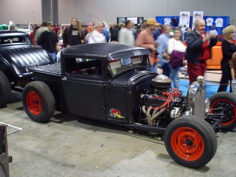 1984 Ford Bronco - A custom black hot rod pickup truck with a prominent engine and bright red wheels is displayed indoors.