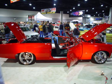 1984 Ford Bronco - A bright red convertible is displayed with its doors and hood open, custom wheels at an auto show.