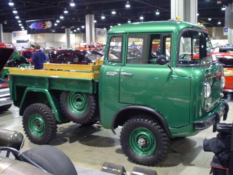 1984 Ford Bronco - A vintage green pickup truck with a wooden bed and dual spare tires is displayed at a car show.