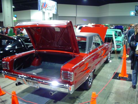1984 Ford Bronco - A red classic car with its trunk open is displayed indoors, with other cars visible in the background.