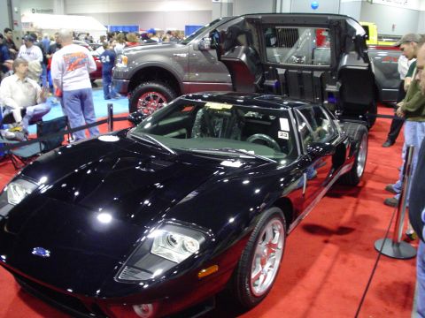 1984 Ford Bronco - A black Ford GT is displayed at a car show, with a modified pickup truck in the background.