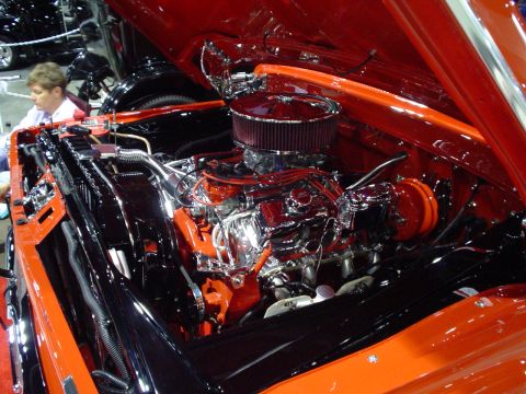 1984 Ford Bronco - The engine compartment of a car is shown with a highly polished V8 engine and custom orange paint.