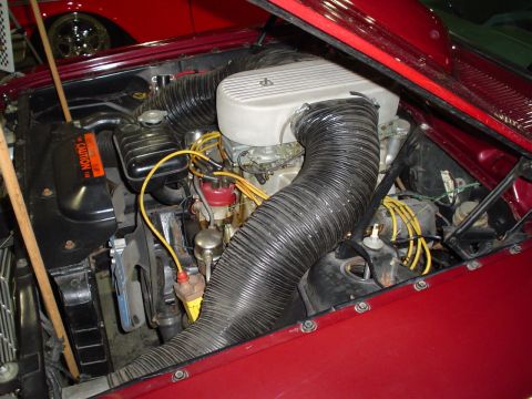 1984 Ford Bronco - Engine bay detail of a red vehicle, with a V8 engine and prominent air intake hoses.