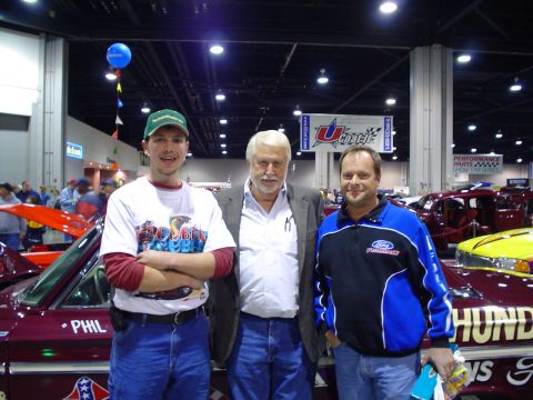 1984 Ford Bronco - Three men pose for a photo at a car show with custom vehicles in the background.