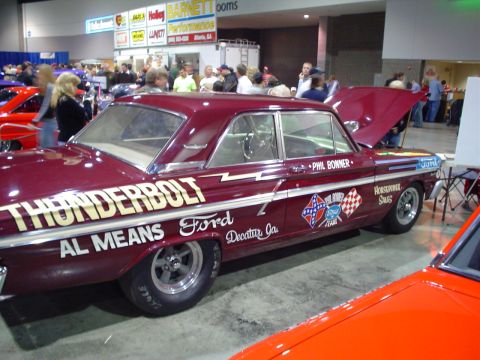 1984 Ford Bronco - A classic Ford Thunderbolt drag car is displayed indoors with its hood open, surrounded by other vehicles and spectators.