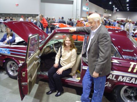 1984 Ford Bronco - A woman sits in a custom maroon car while a man leans on the open door at a car show.