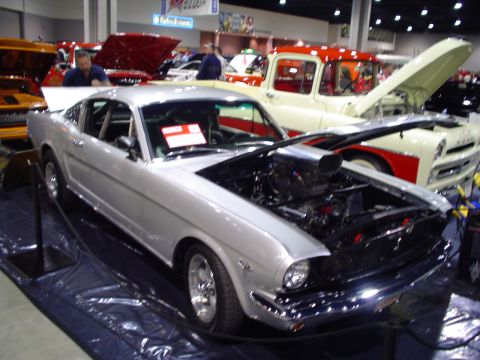 1984 Ford Bronco - Silver 1965 Ford Mustang Fastback displayed at a car show with other vehicles.
