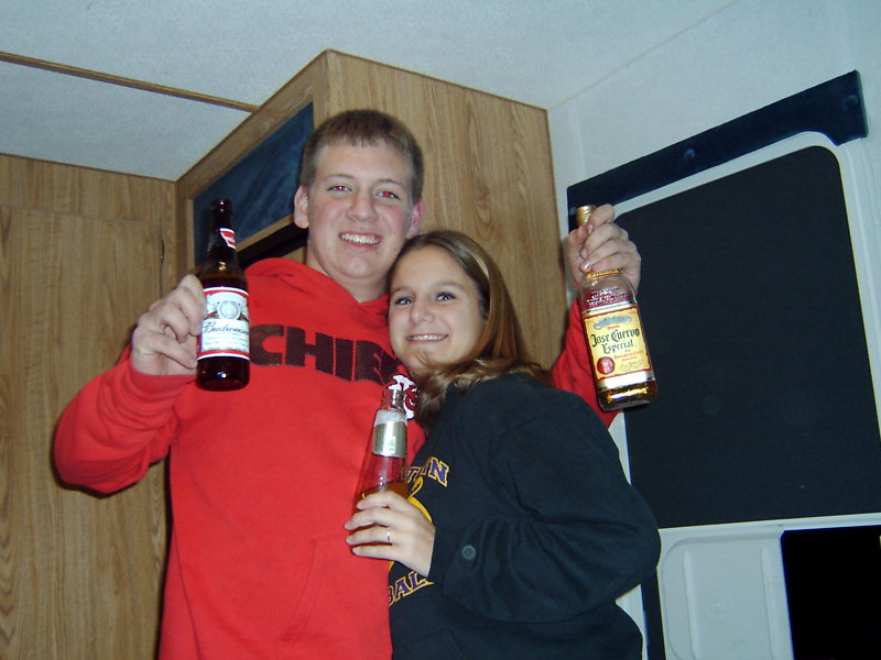 Guy in red hoodie and girl in black shirt holding beer and tequila bottles