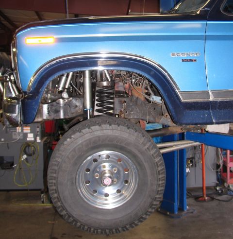 1984 Ford Bronco - Close-up of a blue Ford Bronco's front wheel well and suspension system on a lift.