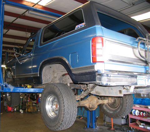 1984 Ford Bronco - This blue Ford Bronco is on a lift, revealing its rear suspension and chrome bumper.