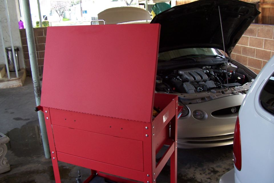 Silver sedan with hood open, showing V6 engine. Red toolbox in foreground