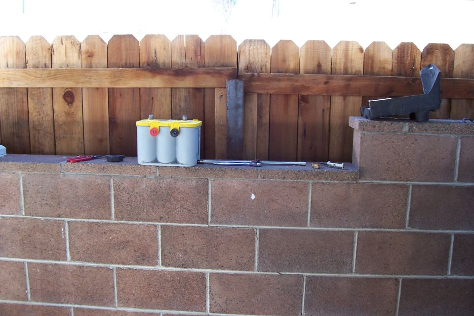 Optima battery on a brick wall in front of a wooden fence