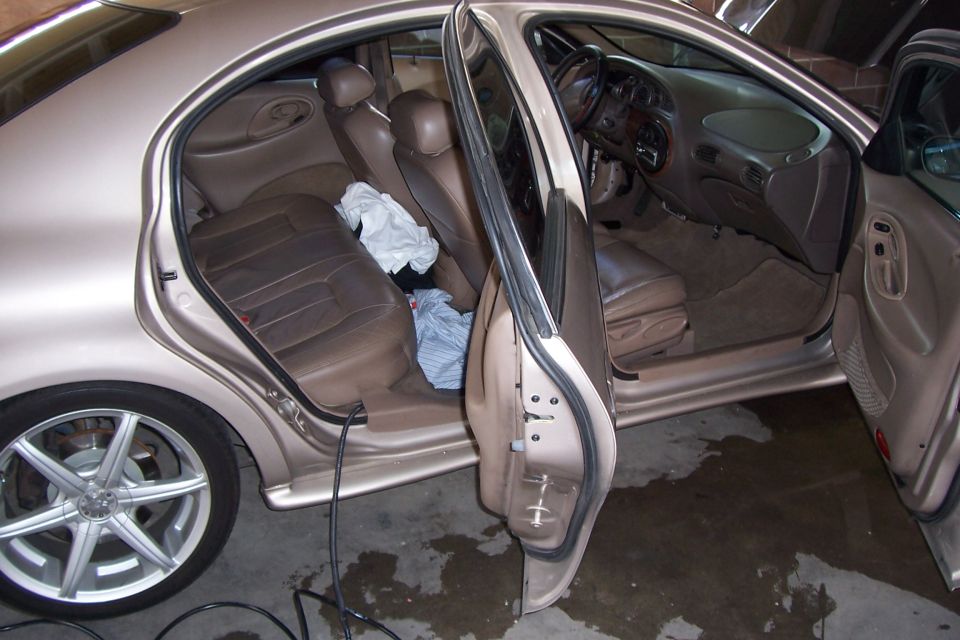 Interior of a beige sedan with brown leather seats and open doors. Clothes are on the back seat