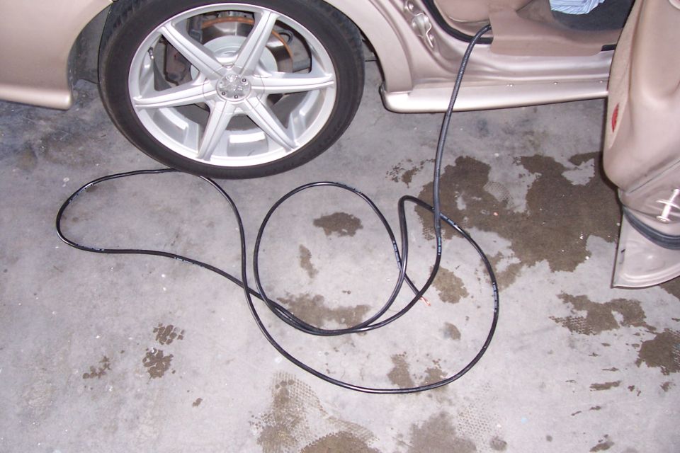 Car door open, showing interior, with a black cable on the concrete floor next to the rear tire