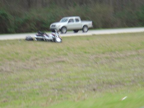 1987 Suzuki Samurai - A motorcycle lies on the grass beside a pickup truck on the side of a road.