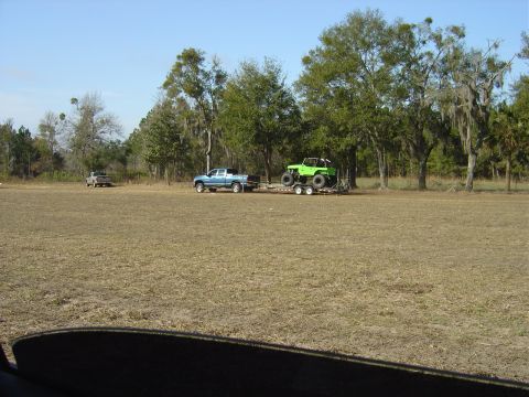 1987 Suzuki Samurai - A blue pickup truck tows a green off-road vehicle on a trailer across a grassy field.