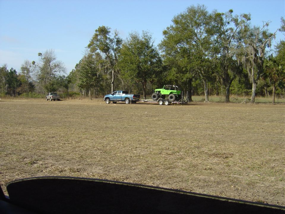 Green off-road vehicle on trailer towed by blue pickup truck