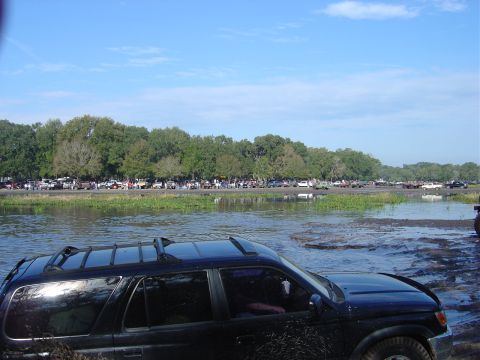 1987 Suzuki Samurai - A line of vehicles is visible in the background, with a black SUV partially submerged in muddy water in the foreground.