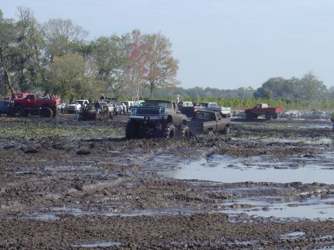 1987 Suzuki Samurai - Multiple trucks are stuck in a muddy field during a mud bogging event.