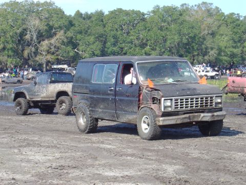 1987 Suzuki Samurai - Two modified off-road vehicles are stuck in the mud at an outdoor event.