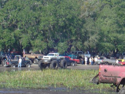 1987 Suzuki Samurai - A muddy field with several trucks, including a large monster truck, gathered for an event.