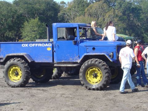1987 Suzuki Samurai - Custom blue off-road truck with oversized tires is parked outdoors with people around it.