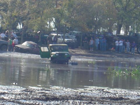 1987 Suzuki Samurai - Off-road vehicles navigate a muddy, watery terrain with spectators watching from the bank.