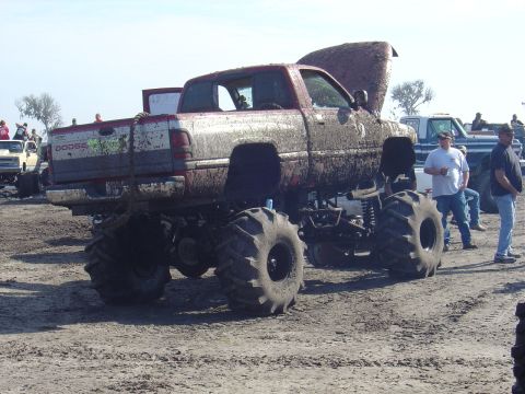1987 Suzuki Samurai - Mud-covered red Dodge pickup truck with lifted suspension and large tires, hood open, at an outdoor event.