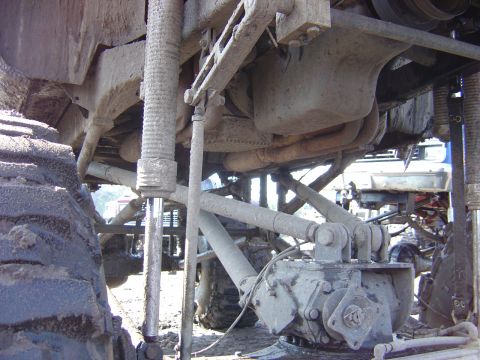 1987 Suzuki Samurai - Close-up of the suspension and drivetrain of a custom off-road vehicle, with another vehicle in the background.