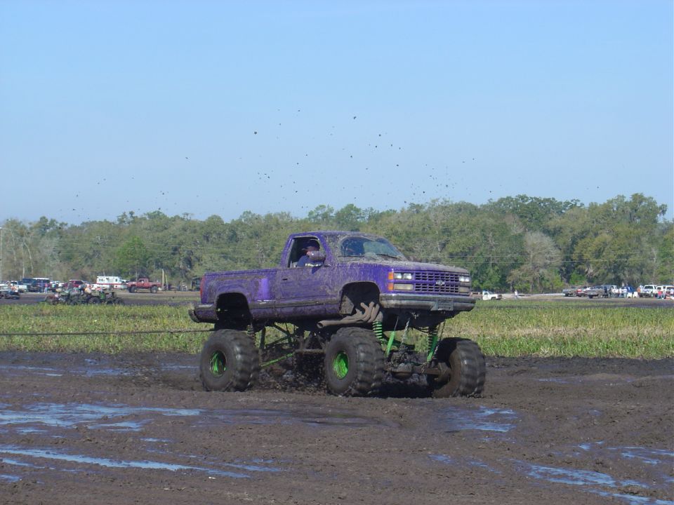 Purple lifted pickup truck driving through mud with large tires