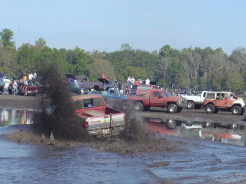 1987 Suzuki Samurai - Multiple trucks are seen participating in a mud bogging event, kicking up large amounts of mud.