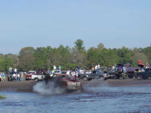 1987 Suzuki Samurai - Trucks churn up mud and water during a competition with onlookers present.