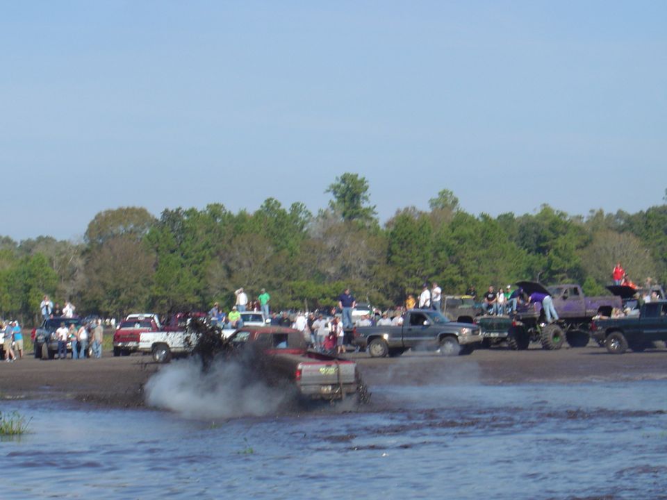 Multiple trucks participating in a mud bog event with spectators watching