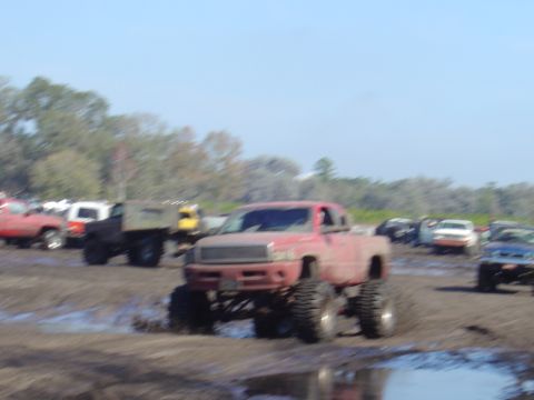 1987 Suzuki Samurai - Several lifted trucks are participating in a mud bogging event on a sunny day.