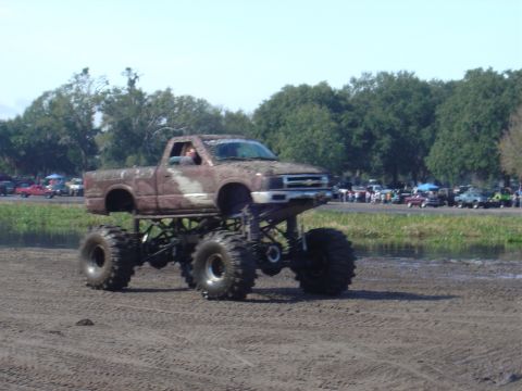 1987 Suzuki Samurai - A heavily modified pickup truck, lifted with oversized tires, navigates a muddy track.