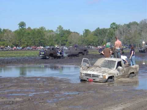 1987 Suzuki Samurai - Multiple trucks are stuck in the mud at an outdoor event.
