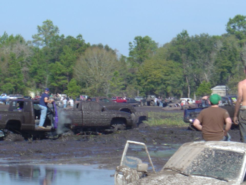 trucks stuck in mud pit with people around